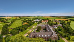 An aerial view of a large estate with expansive green fields, a golf course, and a prominent building with multiple wings.