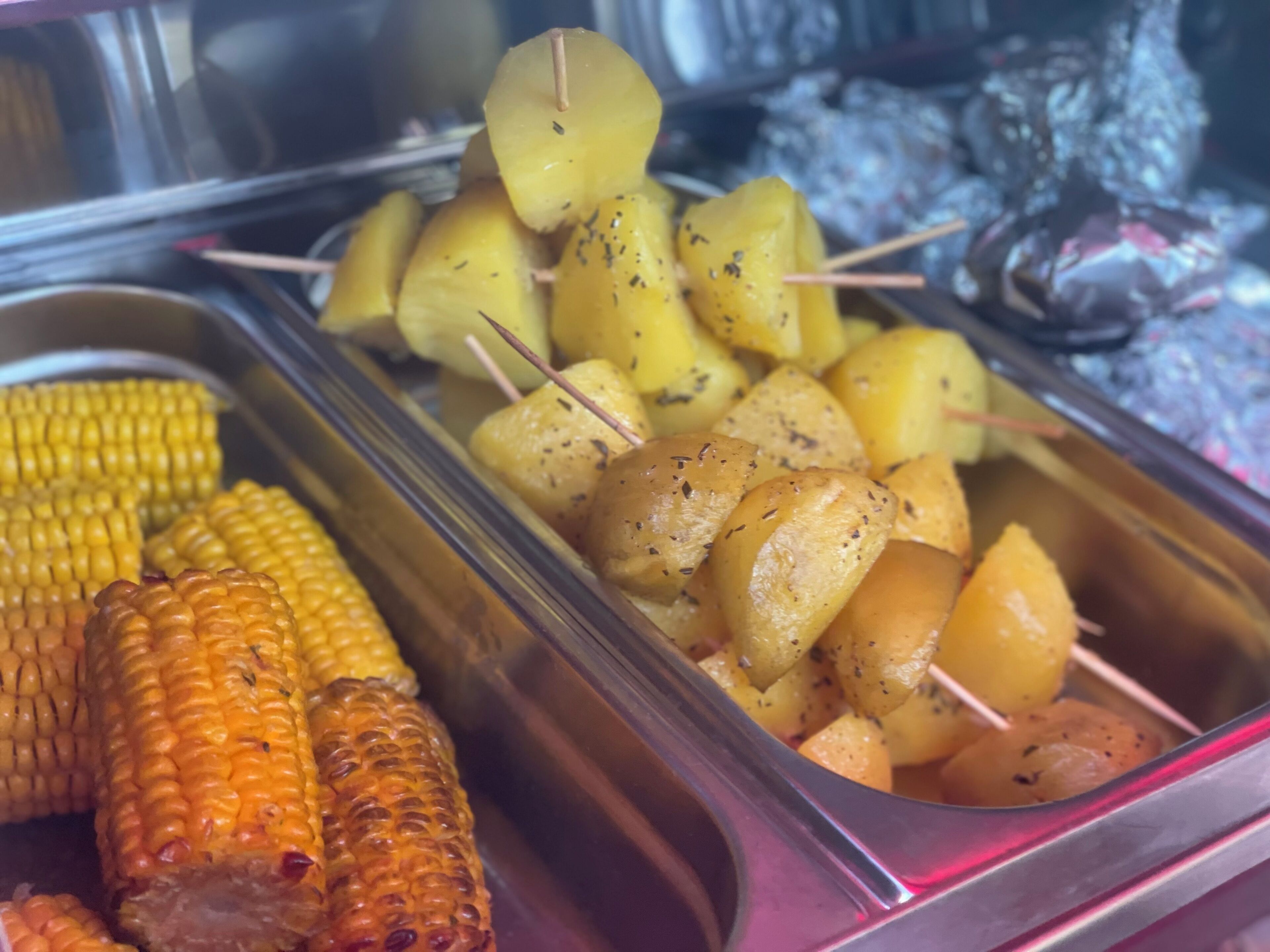 A buffet with corn on the cob, roasted potatoes, and grilled chicken.