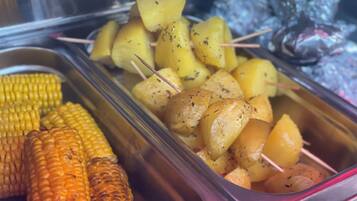 A buffet with corn on the cob, roasted potatoes, and grilled chicken.