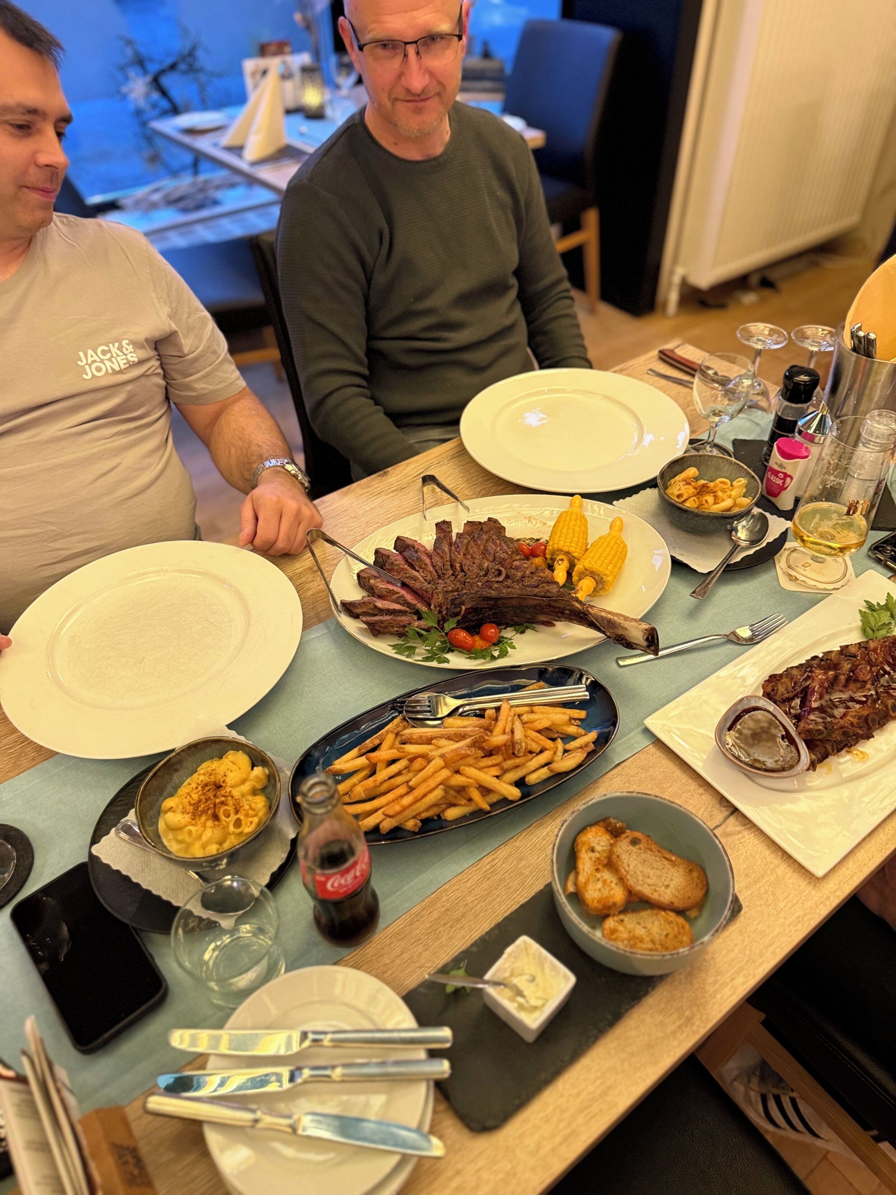 A dining table with various dishes, including steak, corn, and pasta.