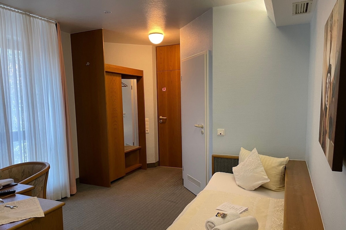 A hotel room with a bed, a desk, a chair, a wardrobe, and a bathroom door.