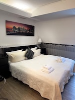 Una cama impecable con almohadas, un cuadro con un paisaje urbano, una lámpara y una pared decorada con motivos urbanos.