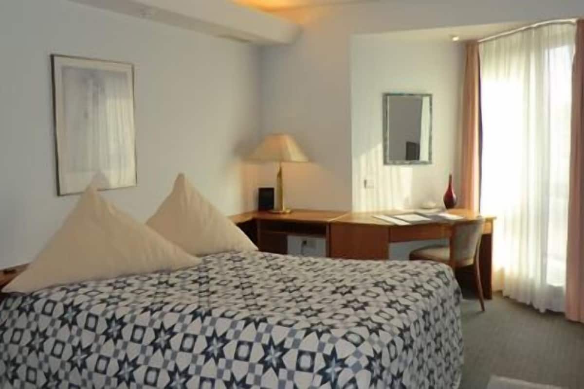 A hotel room with a bed, desk, chair, TV, and curtains.