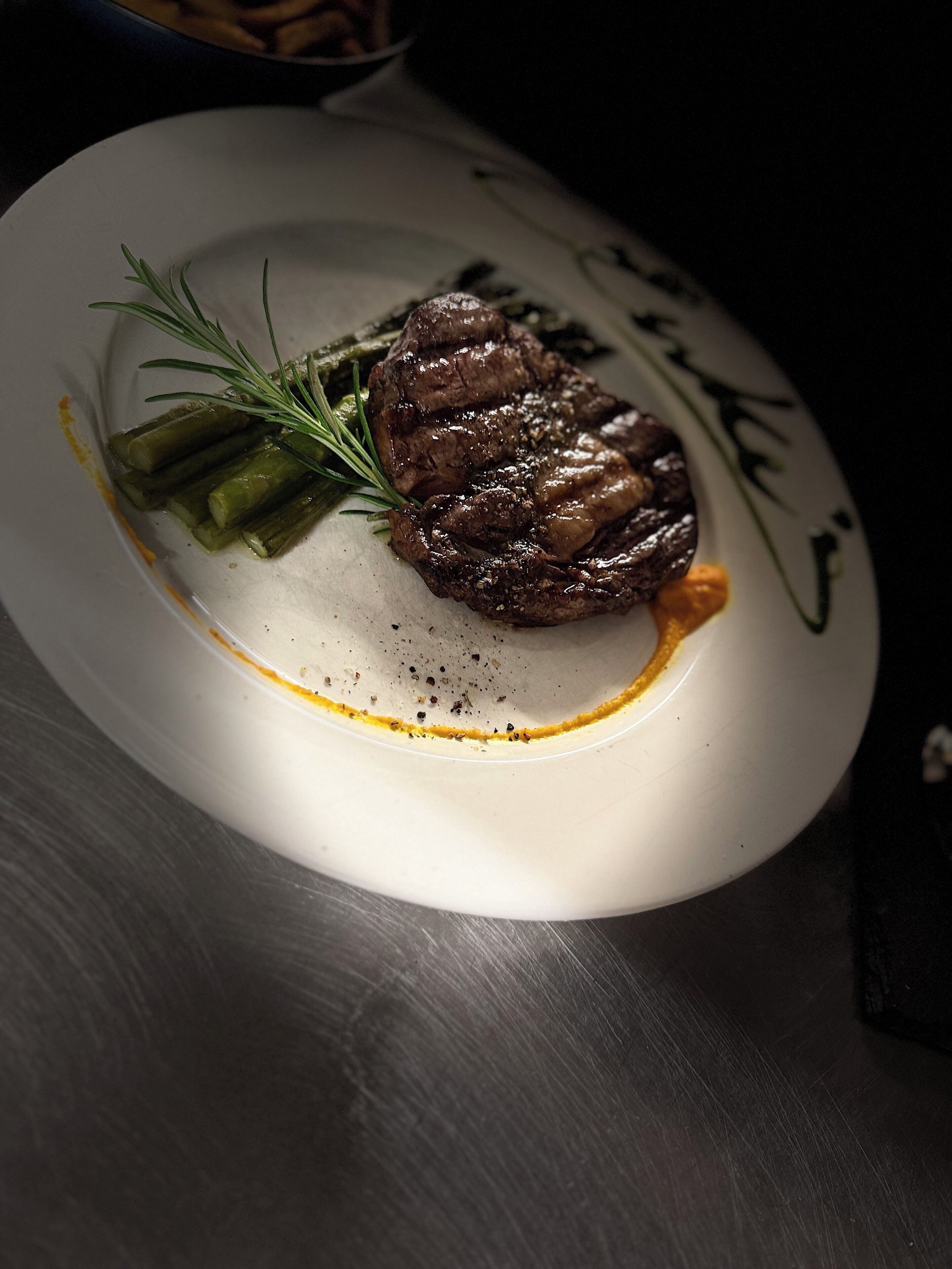 A plate with a steak, asparagus, and a garnish on a white plate.