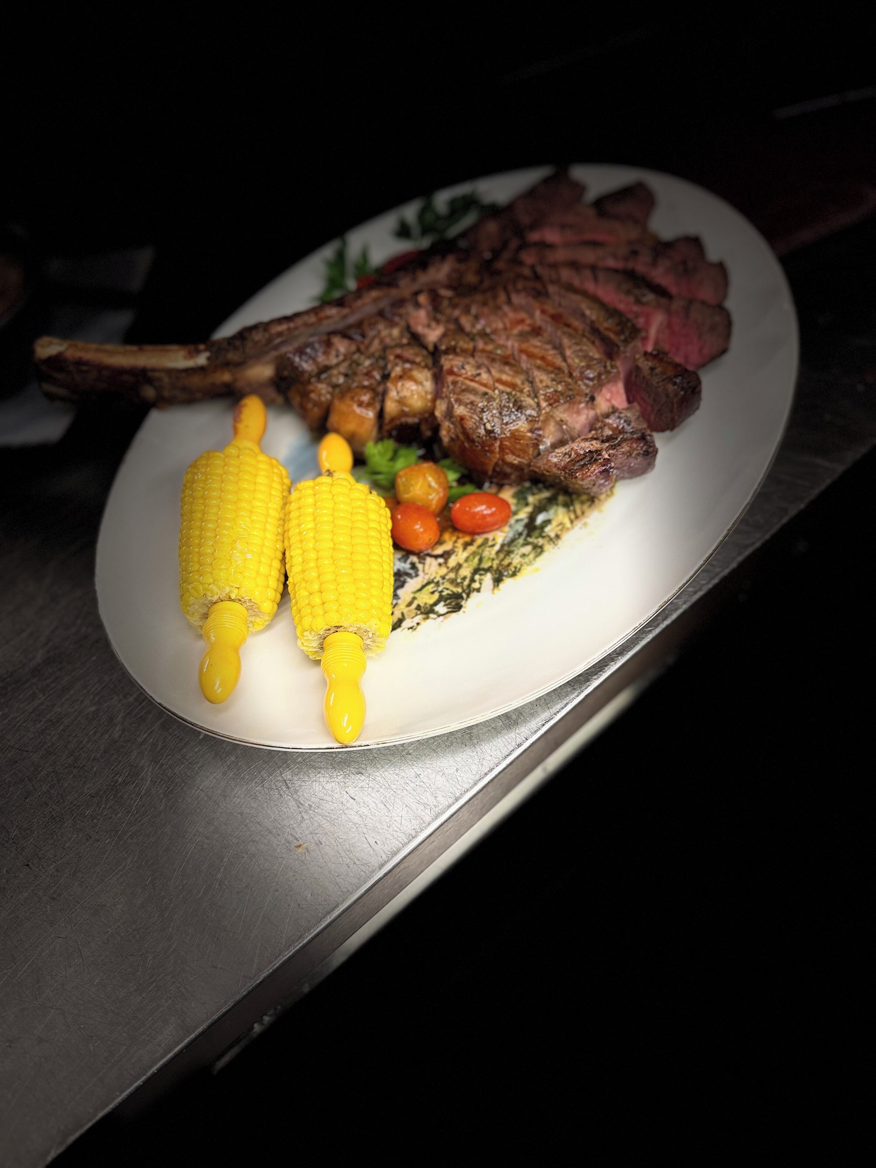 Un plato con filete a la parrilla, mazorca y verduras pequeñas.