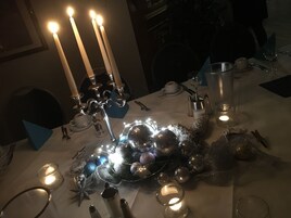 Una mesa preparada para una comida, con velas, una jarra de vidrio y un centro de mesa decorativo.
