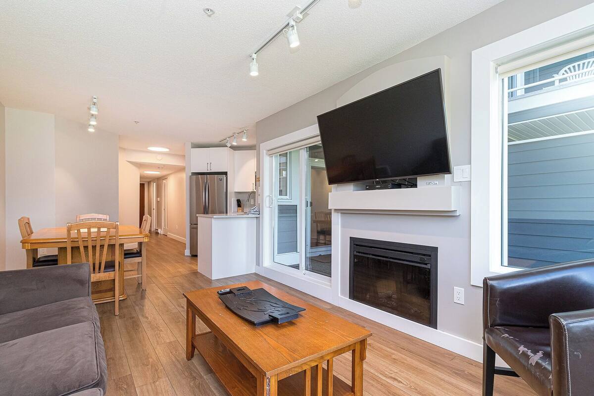 A modern living room with a fireplace, a flat-screen TV mounted above it, and a dining area with wooden furniture.
