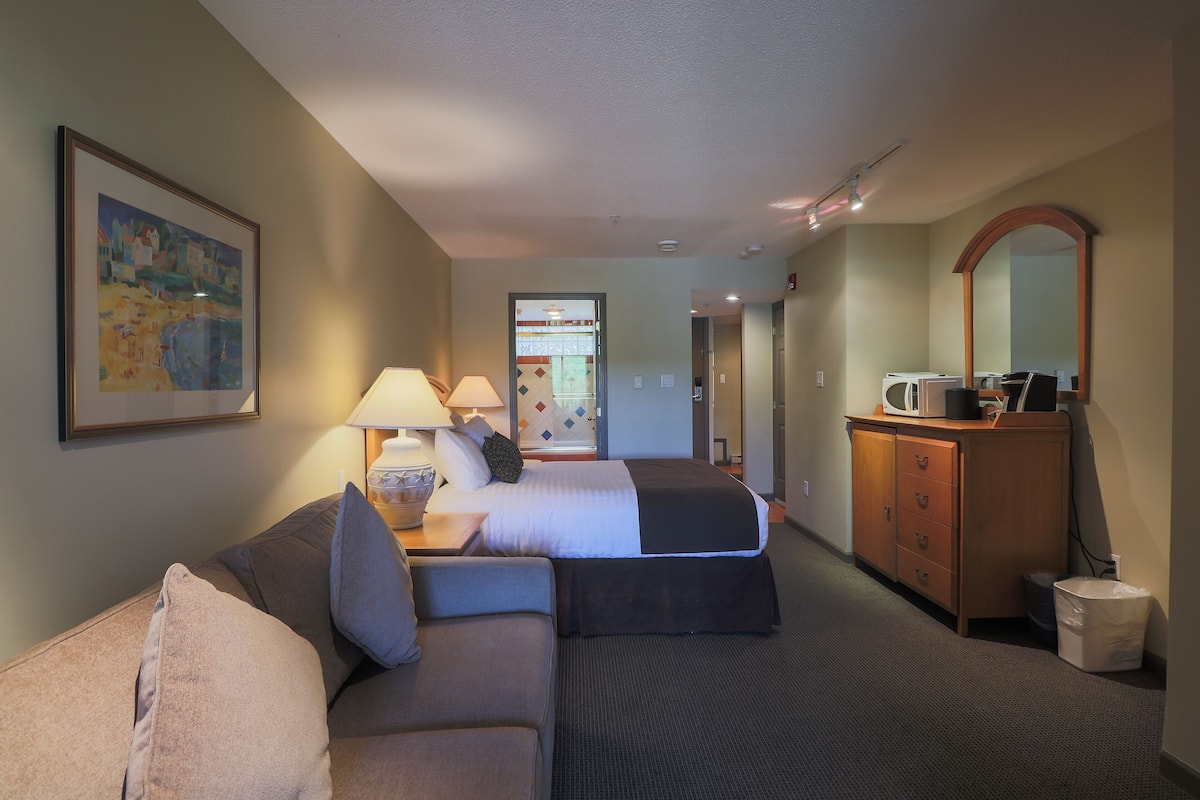 A hotel room with a bed, a sofa, a dresser, a mirror, and a painting on the wall.