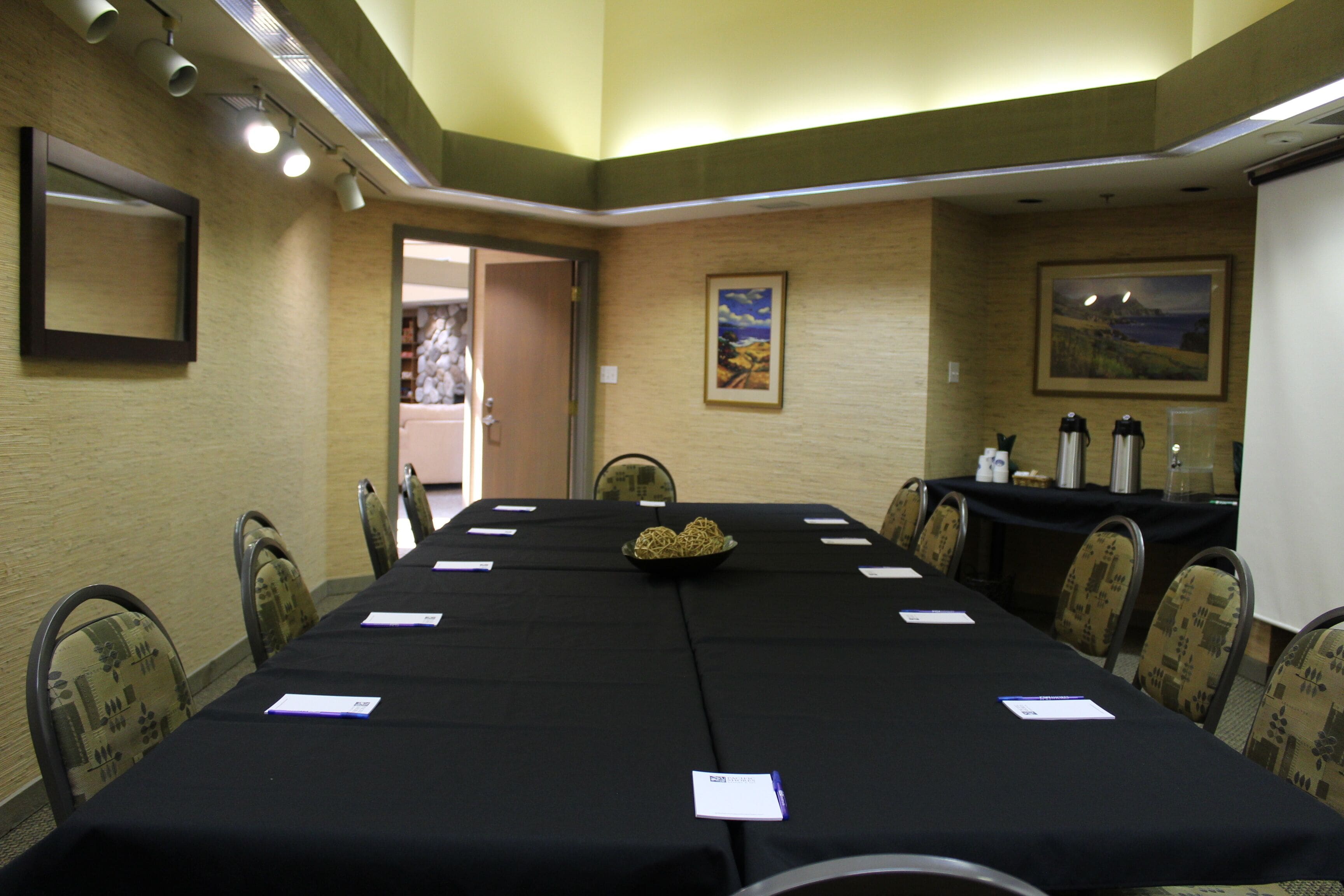 A conference room with a long table, chairs, name cards, and a projector screen.