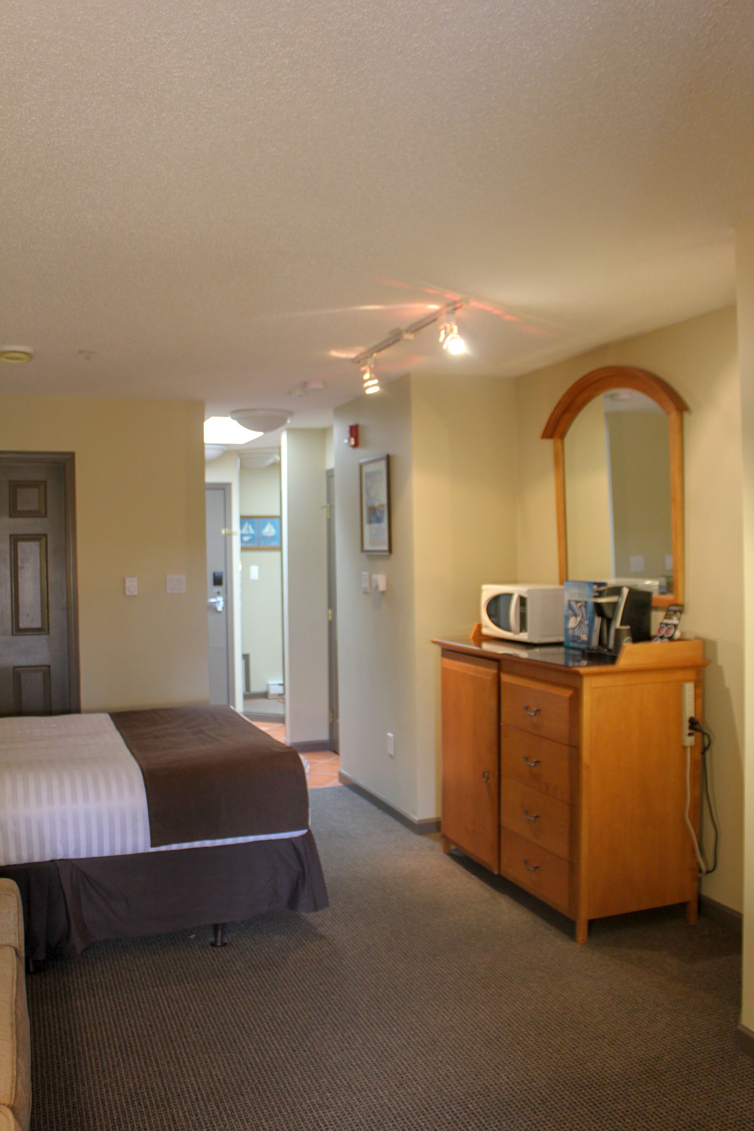 A hotel room with a bed, a wooden dresser, a microwave, and a mirror.