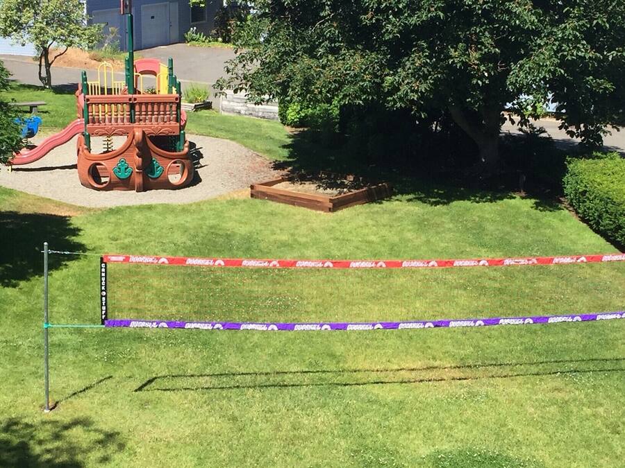 Ein Spielplatz mit Rutsche und Klettergerüsten, umgeben von Gras und Bäumen.