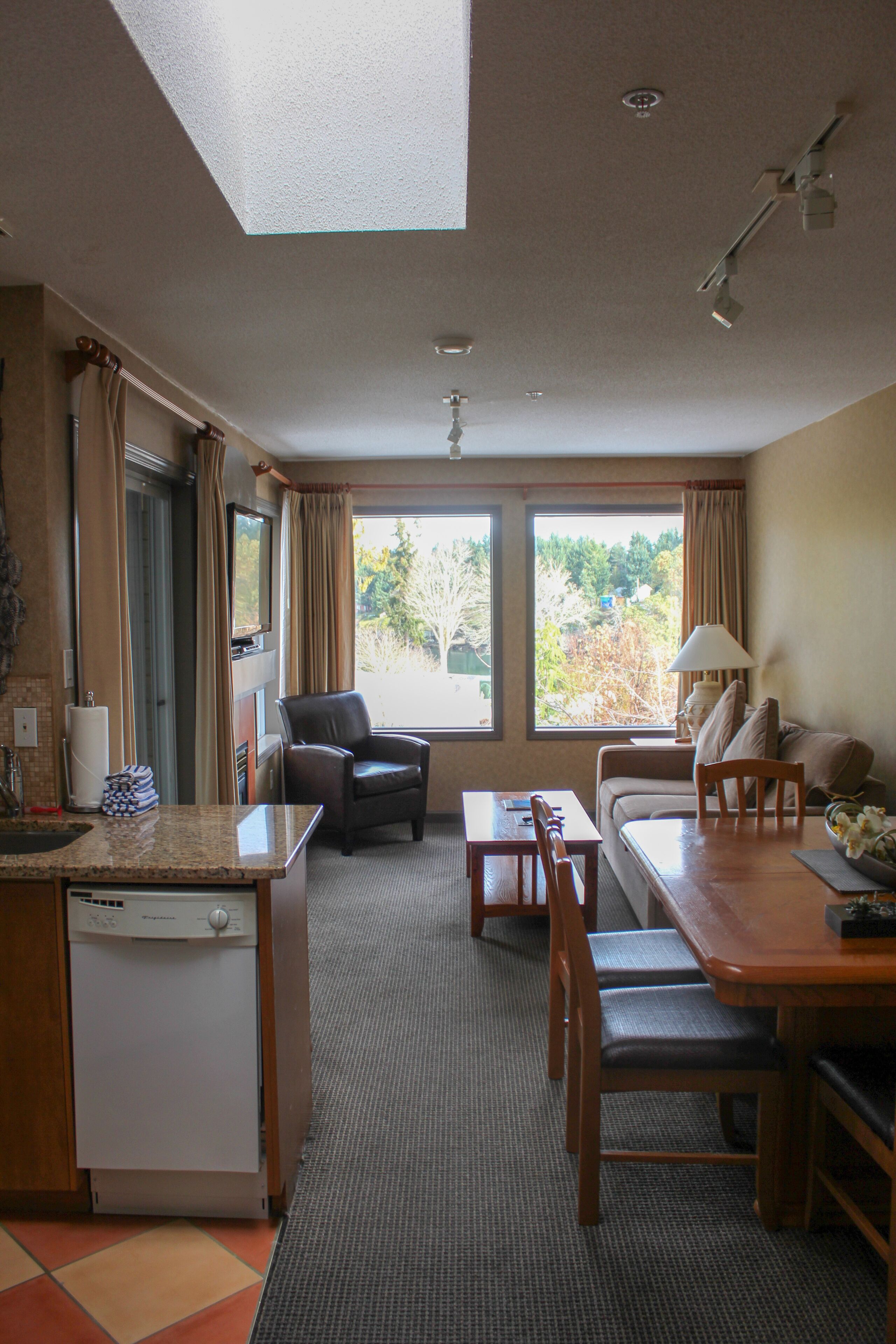 A compact hotel room with a kitchenette, a dining area, and a seating area with a view of the outdoors.