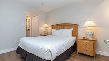 Una cama bien hecha con cabecera de madera, dos mesitas de noche con lámparas y una cómoda de madera con cajones.