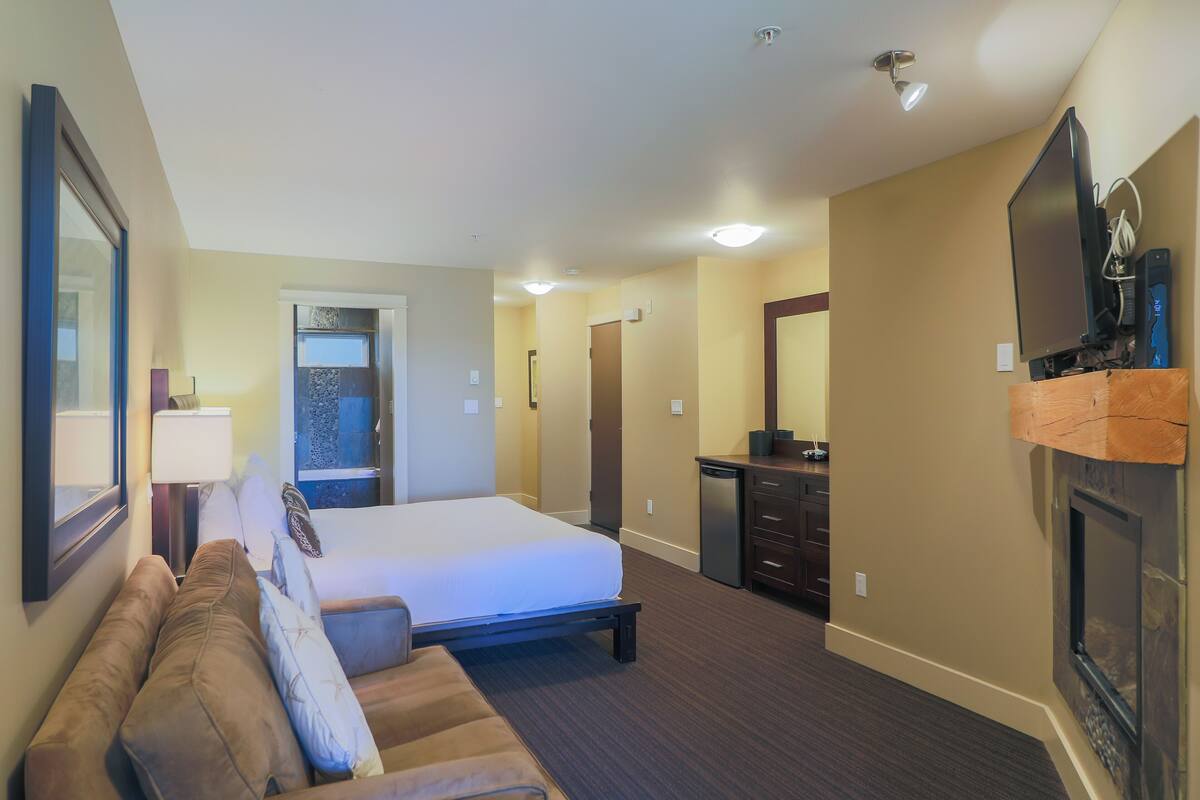 A hotel room with a bed, a sofa, a TV, a fireplace, and a desk.