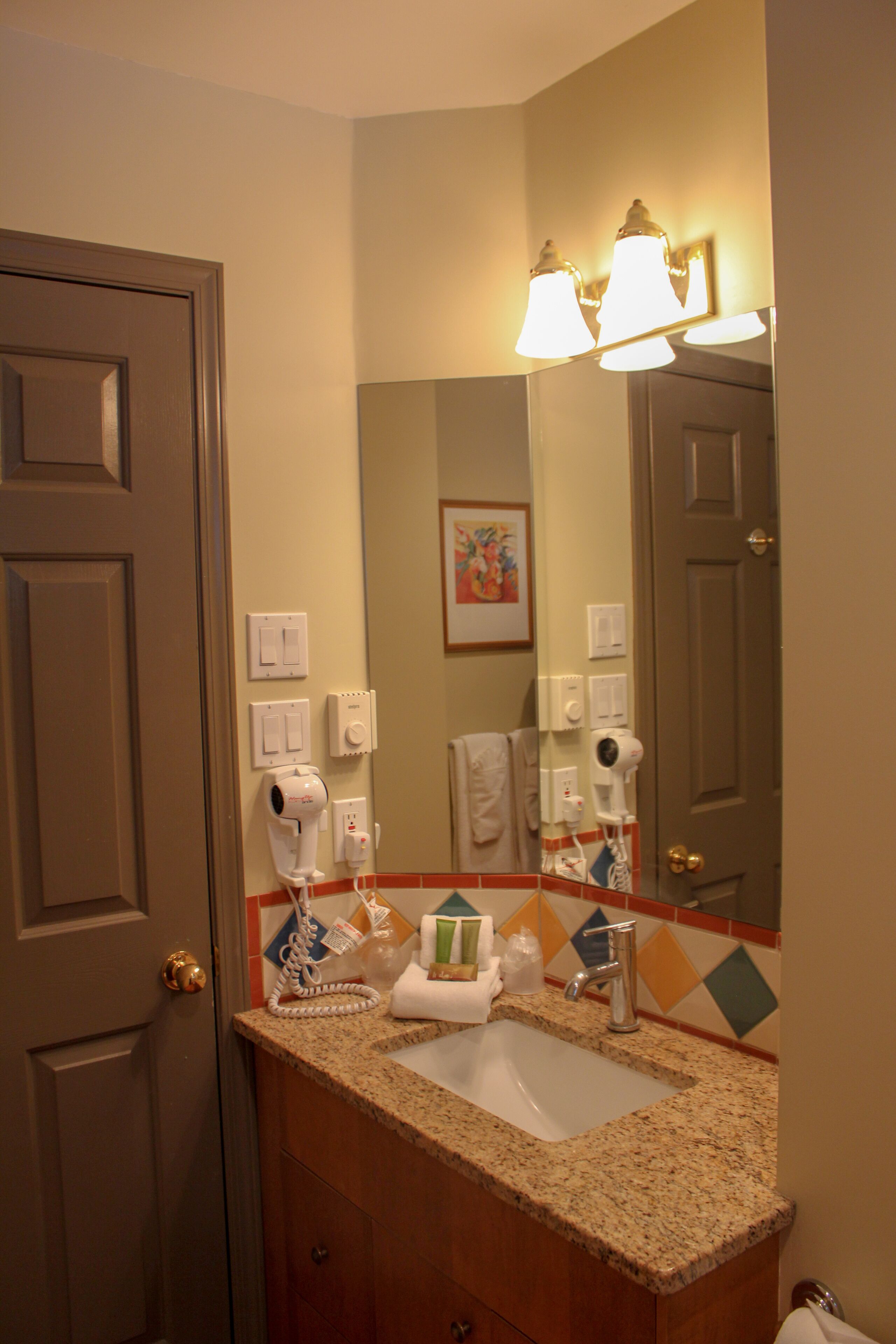 A bathroom with a sink, mirror, and towel rack. There are light switches and a hairdryer on the wall.