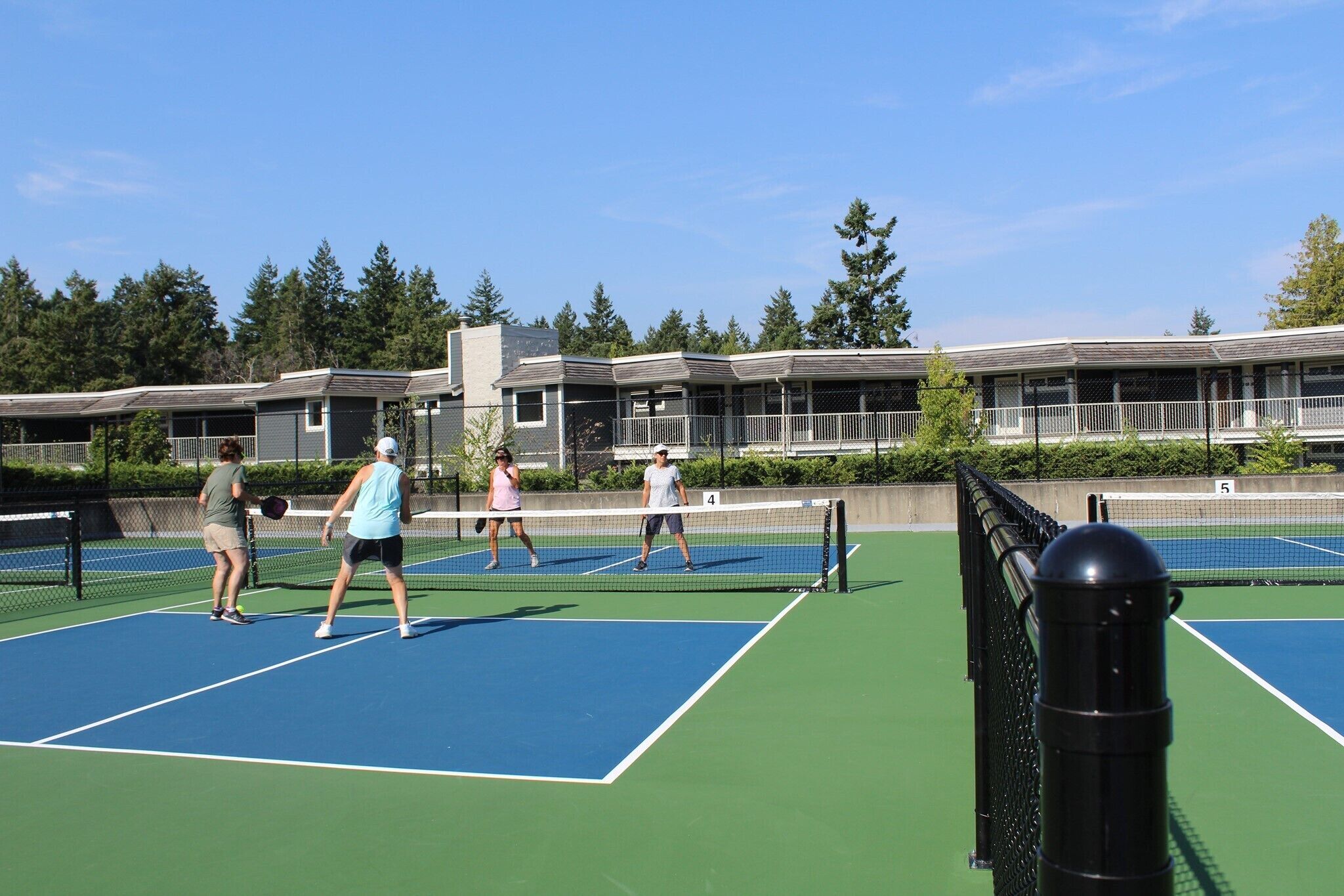 Een tennisbaan met vier spelers, omringd door een hek en bomen.