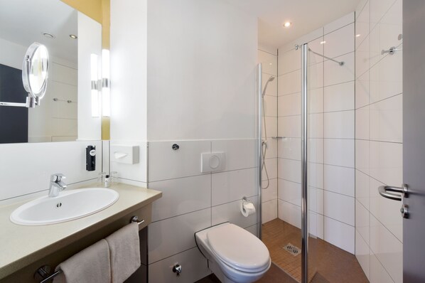 A modern bathroom with a sink, toilet, and glass-enclosed shower. - KOOS Hotel&Apartments (Munich)