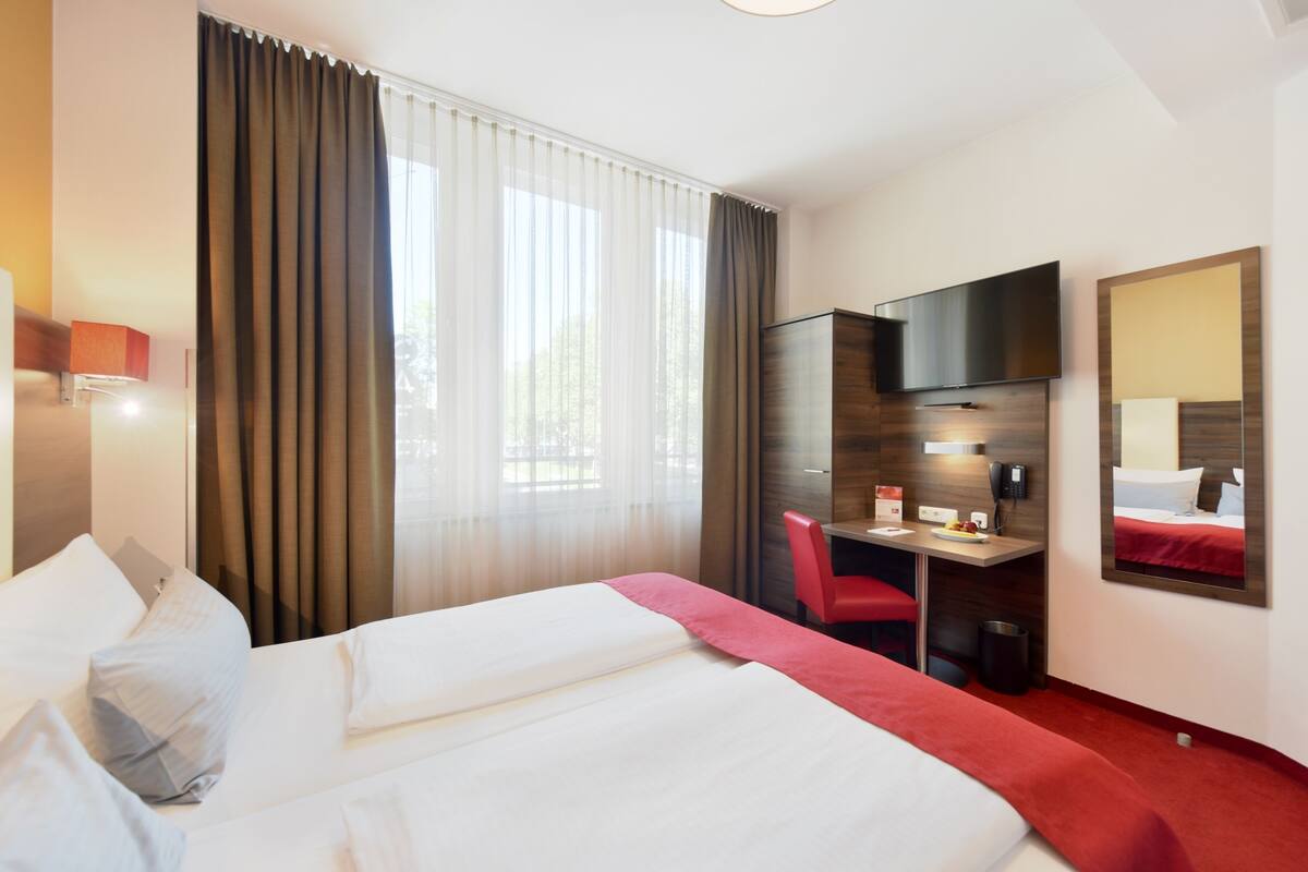 A hotel room with two beds, a desk, a chair, a TV, and a mirror.
