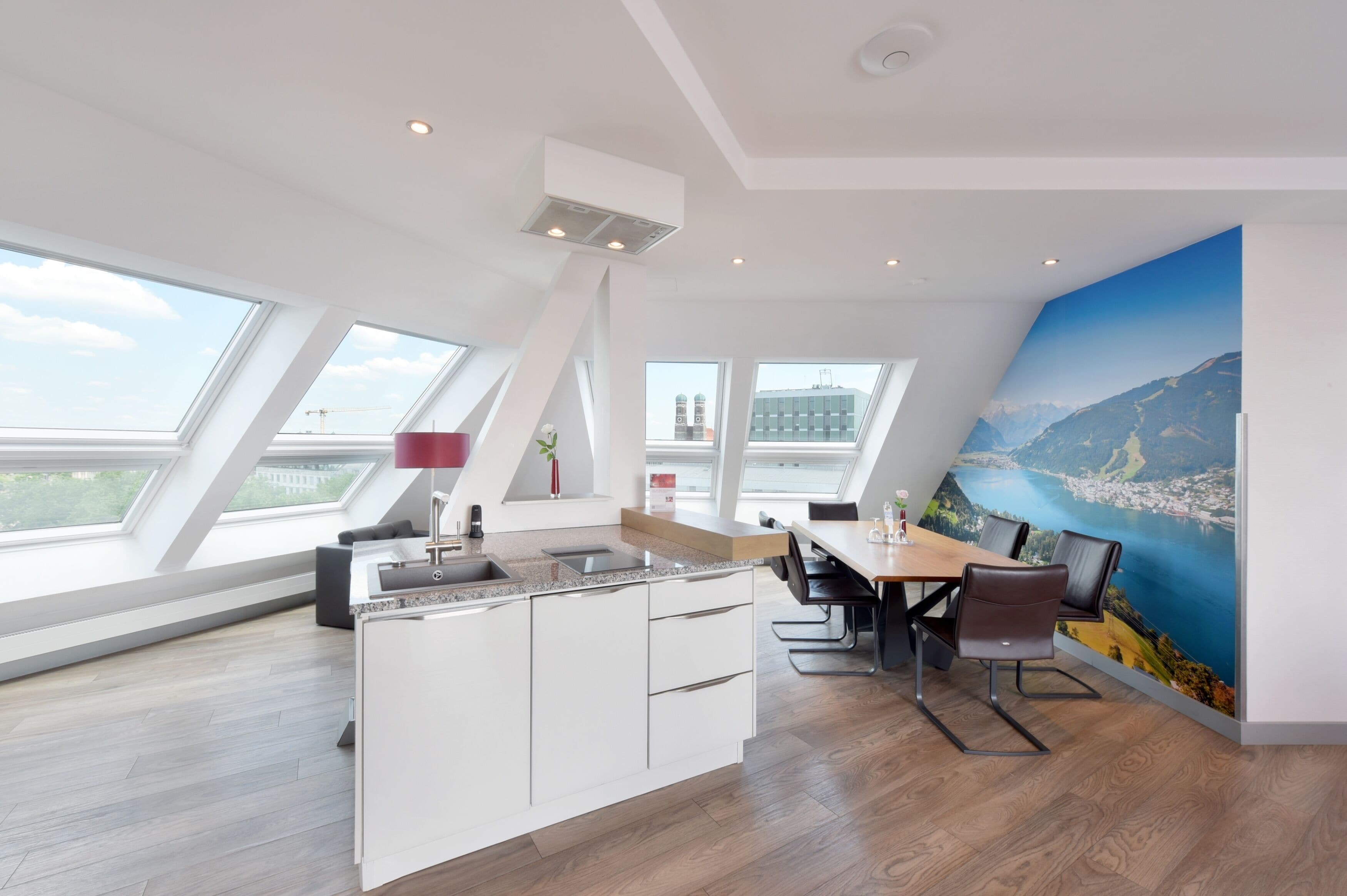 Una cocina moderna con una isla central, una zona de comedor con mesa y sillas, y ventanas amplias con vistas a la ciudad.