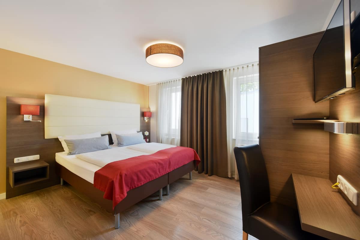 A modern hotel room with a large bed, bedside tables, a desk, and a TV.