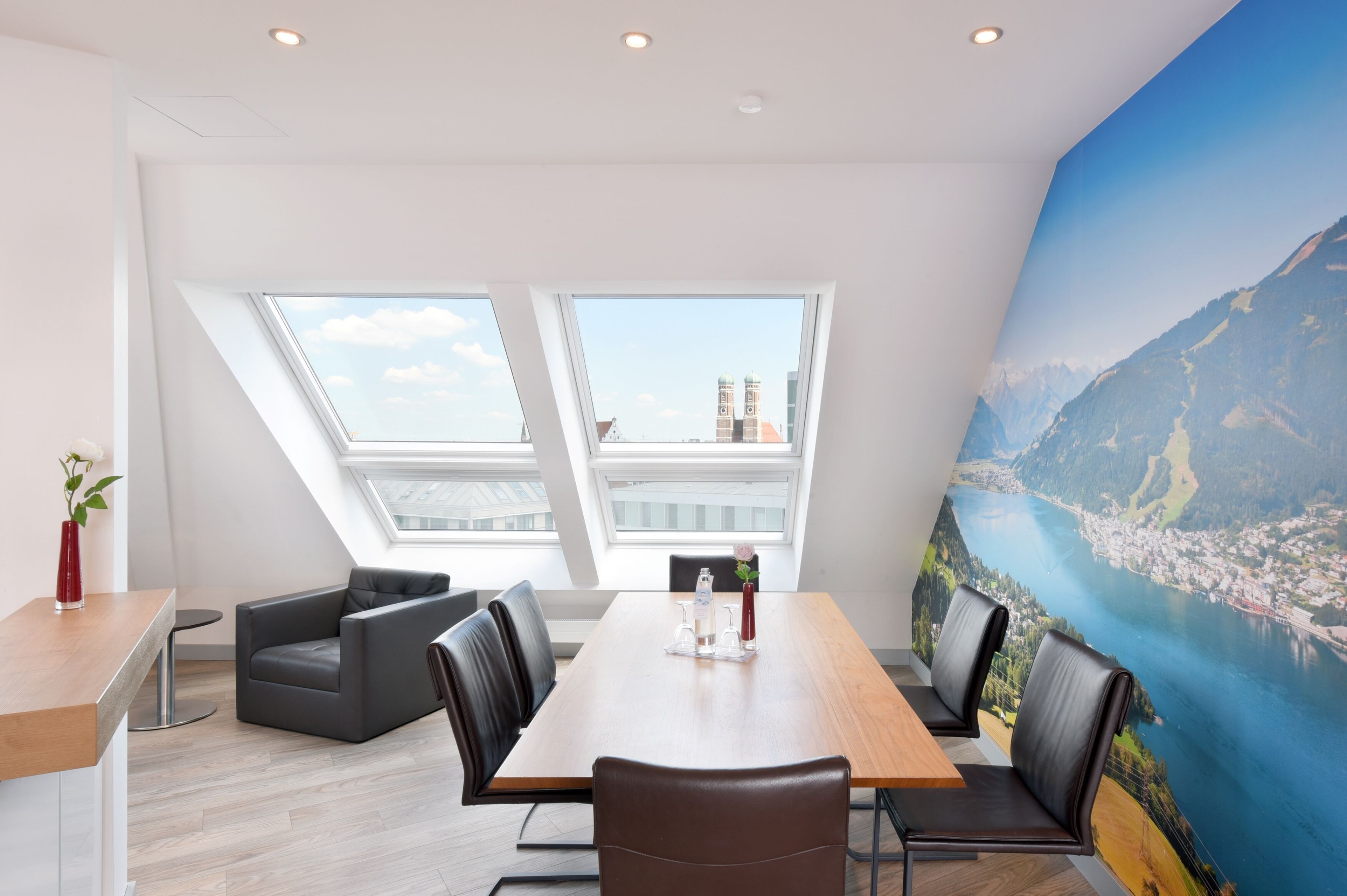 A modern meeting room with a wooden table, leather chairs, and a large mural of a scenic landscape.