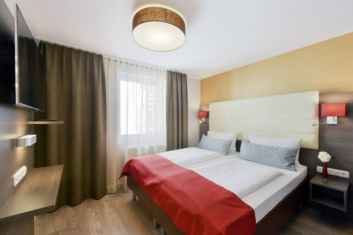 A hotel room with a bed, a TV, a bedside table, a nightstand, and a lamp.