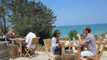 An outdoor seating area with wooden tables and chairs, overlooking a scenic view of the sea.