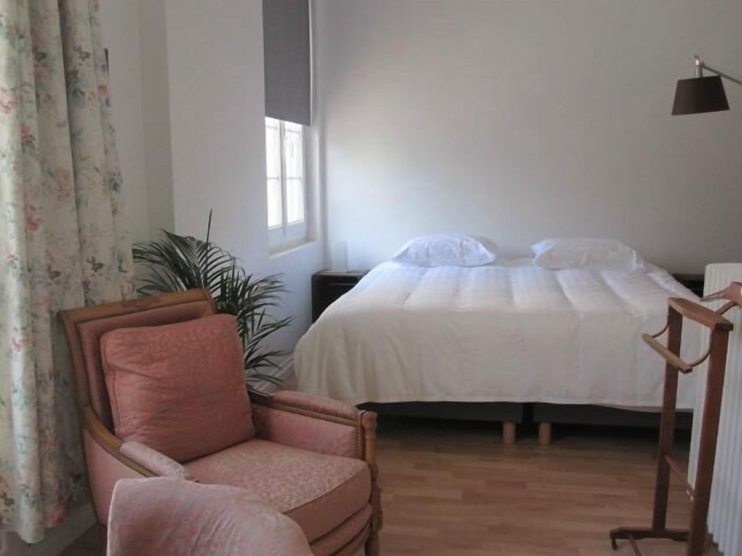 A bedroom with a bed, a chair, a bedside table, a lamp, and a window.