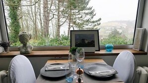 A dining table set with plates, cutlery, and wine glasses, with a view of trees and a cityscape through a window. - Auberge du vieux puits (Dieppe)
