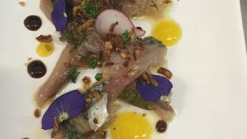 A white plate with a dish consisting of fish, radish slices, and garnishes.