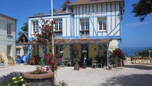 A two-story building with a blue and white facade, a balcony with hanging plants, and a gravel courtyard with flowers. - Auberge du vieux puits (Dieppe)