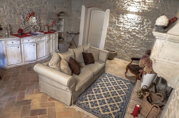 A living room with a stone wall, a white sofa, a patterned rug, and a fireplace. - Corte San Ruffillo-Azienda Agrituristica (Dovadola)