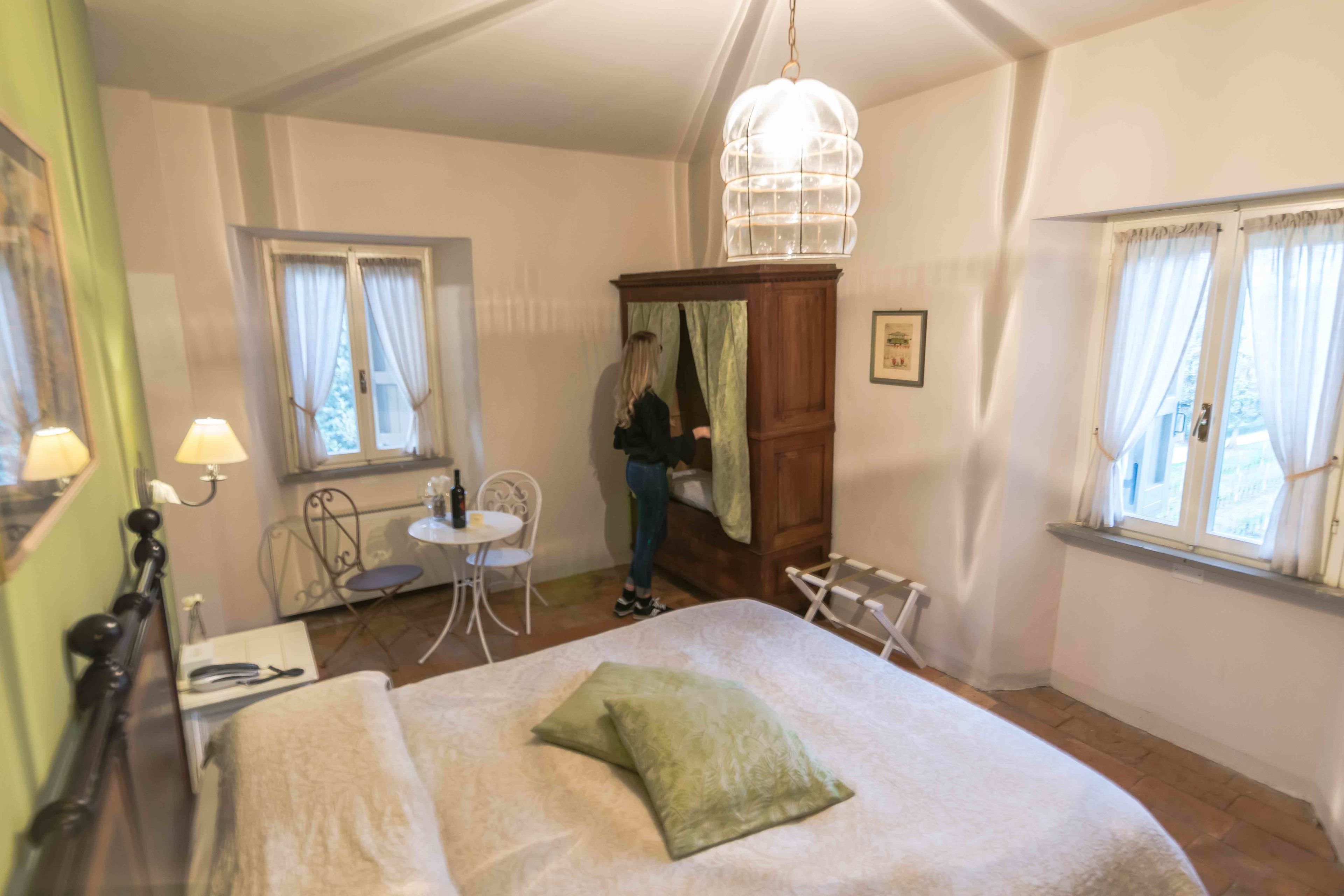Una camera da letto con un letto, un'armadietto in legno, una lampada a sospensione, un tavolino e una sedia.