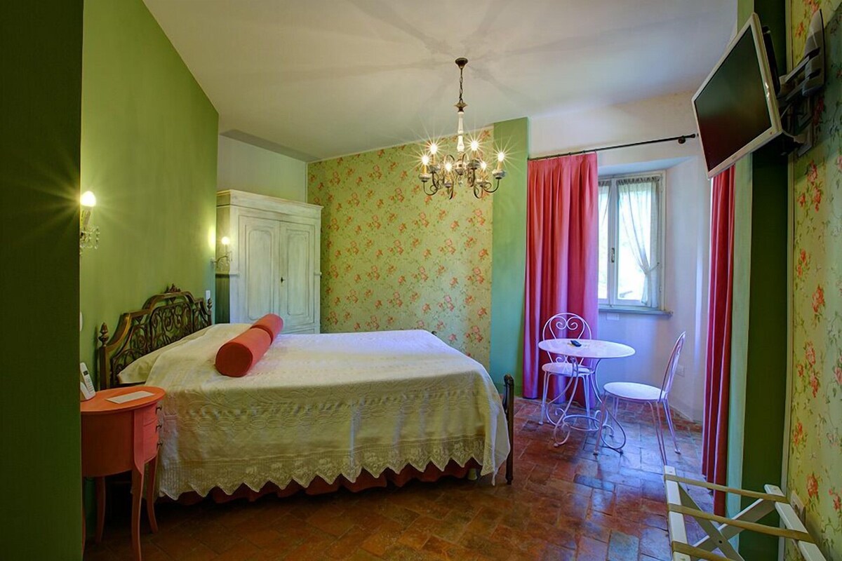 A bedroom with a bed, a desk, a chair, a TV, and a window with curtains.