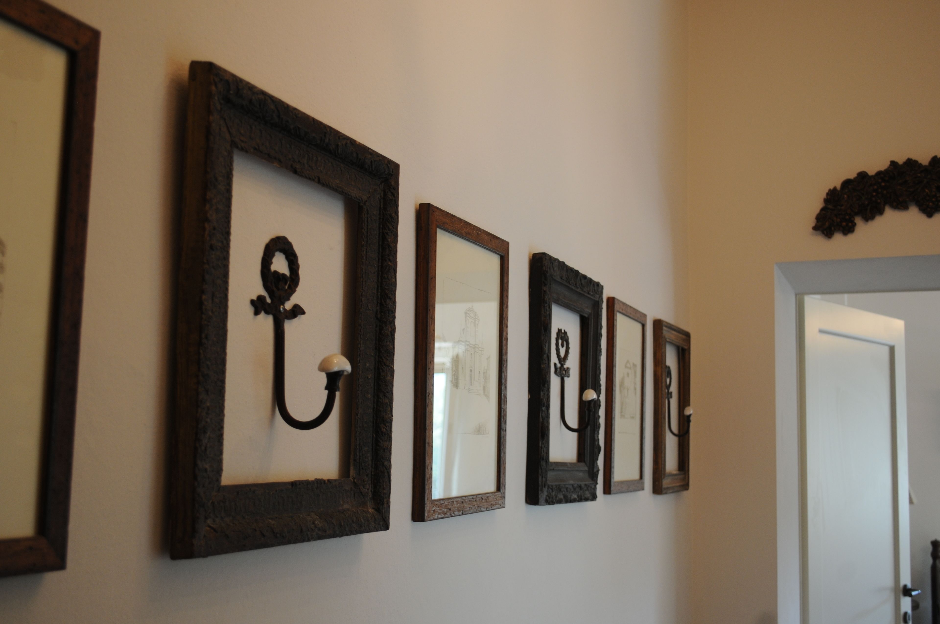 Um corredor com quatro obras emolduradas na parede, uma porta à direita e um detalhe decorativo acima da porta.
