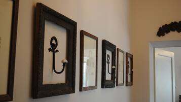 Um corredor com quatro obras emolduradas na parede, uma porta à direita e um detalhe decorativo acima da porta.