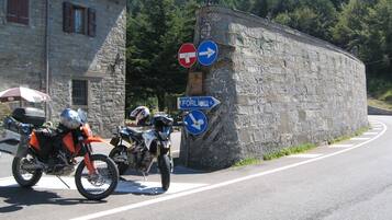 A stone building with a motorcycle parked in front, a 'no entry' sign, and directional signs for 'FORLI' and 'FORLI 53'.