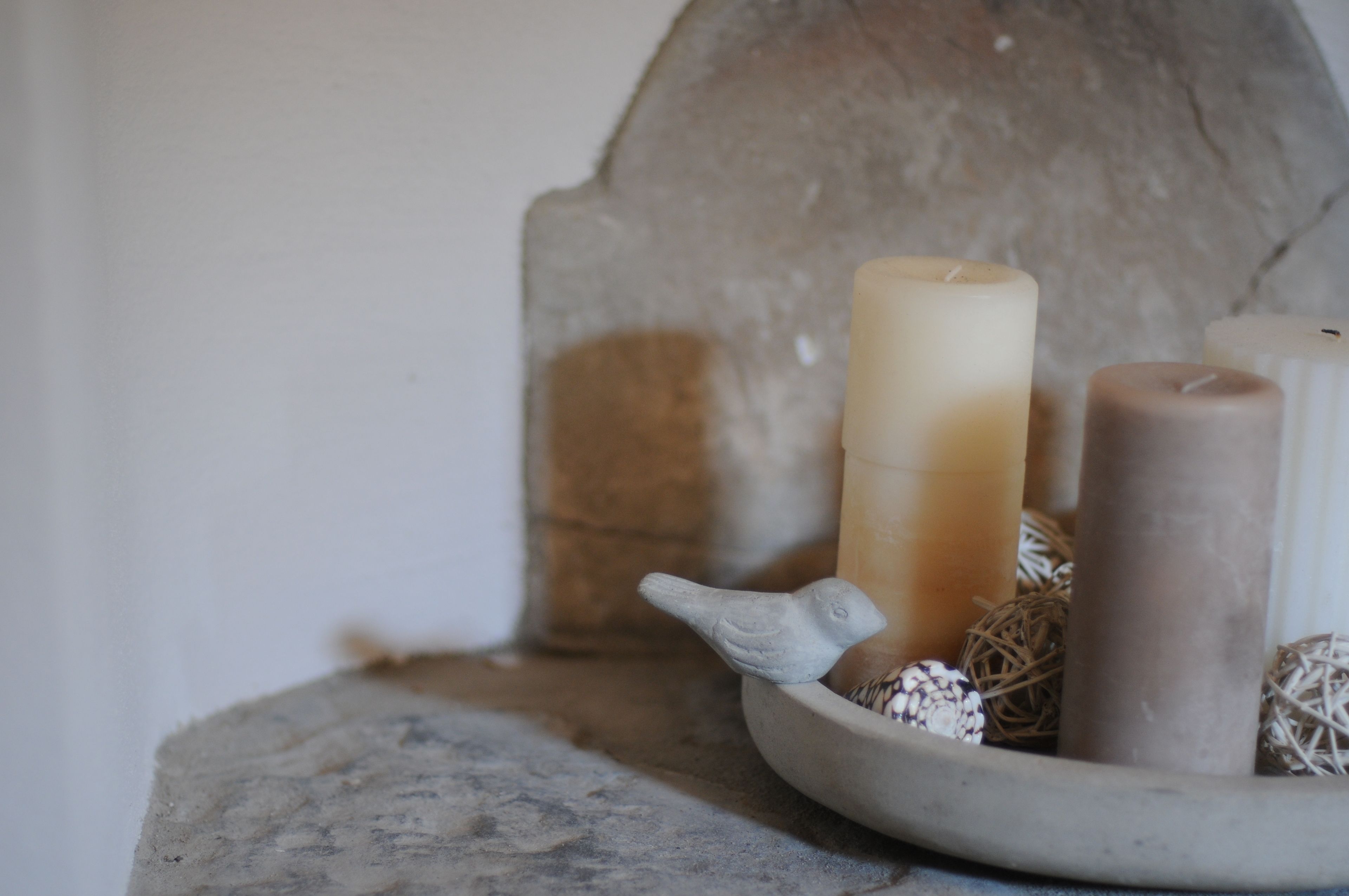 Un mur de pierres, des bougies et une statuette d’oiseau posés sur une table.