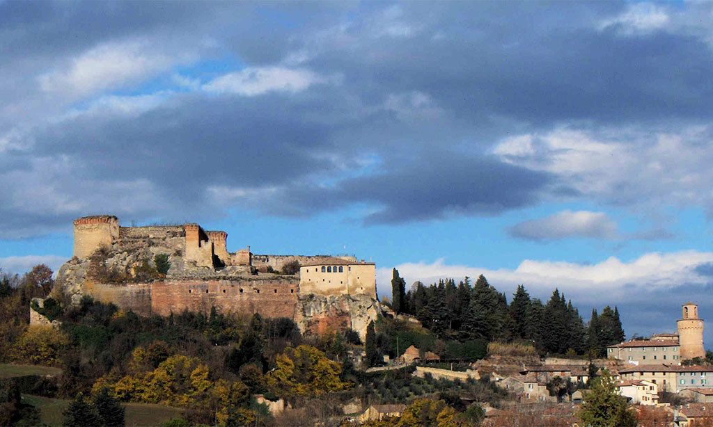 Un château historique perché sur une colline, surplombant une ville, entouré d’arbres et sous un ciel nuageux.