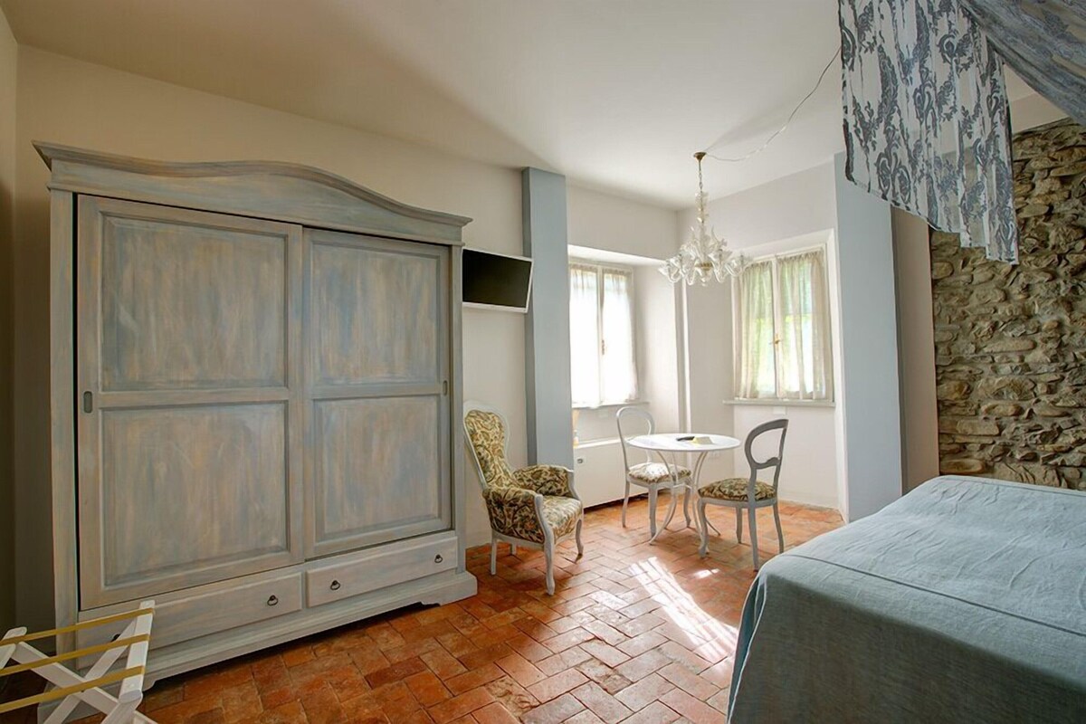 A room with a large wardrobe, a dining table with chairs, a chandelier, and a stone wall.