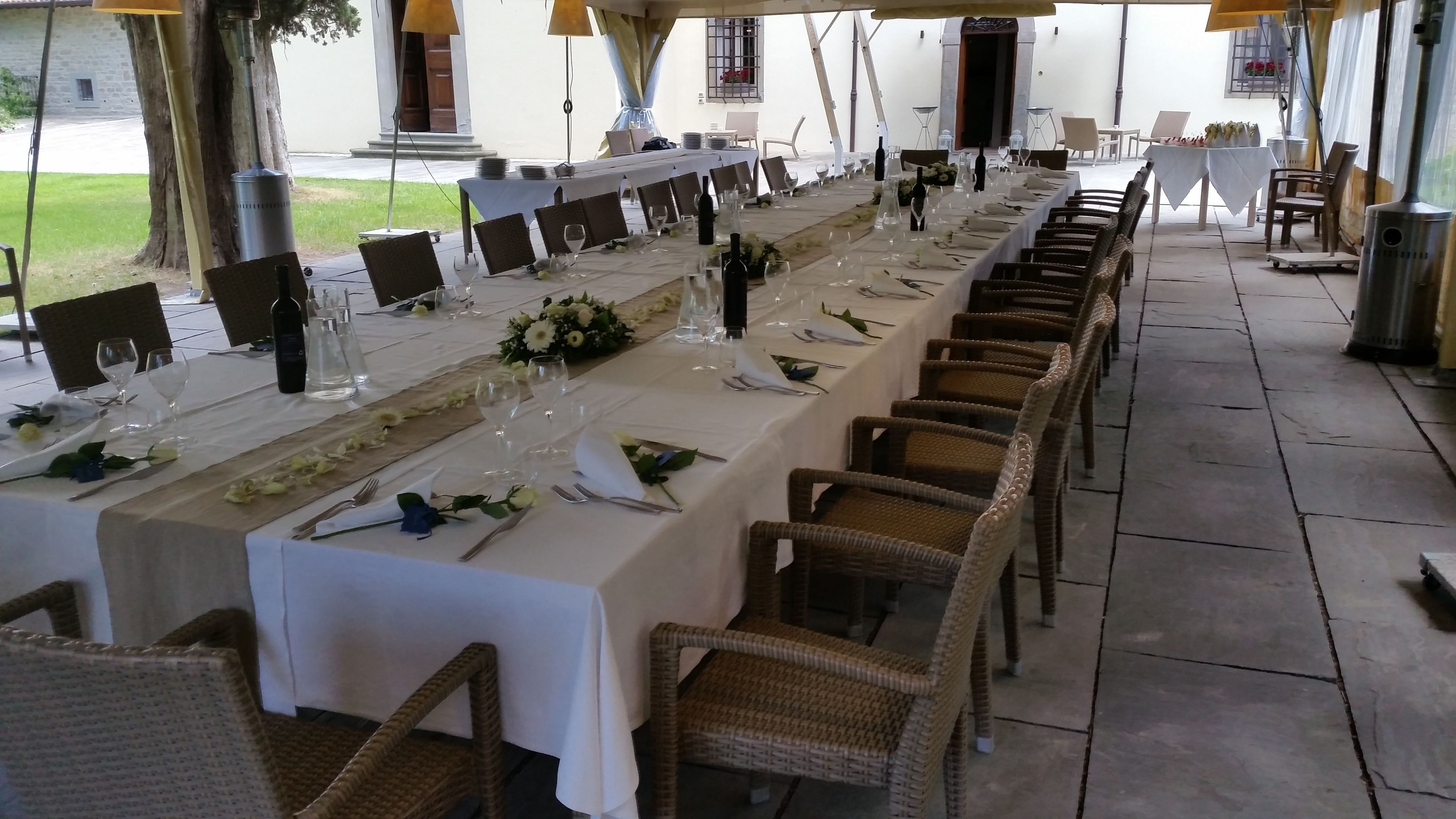 Une longue table à manger, entourée de chaises en osier, recouverte de nappes blanches et agrémentée de verres à vin.