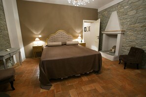 Un dormitorio con una cama grande, una chimenea de piedra y una mesita de noche con lámpara.