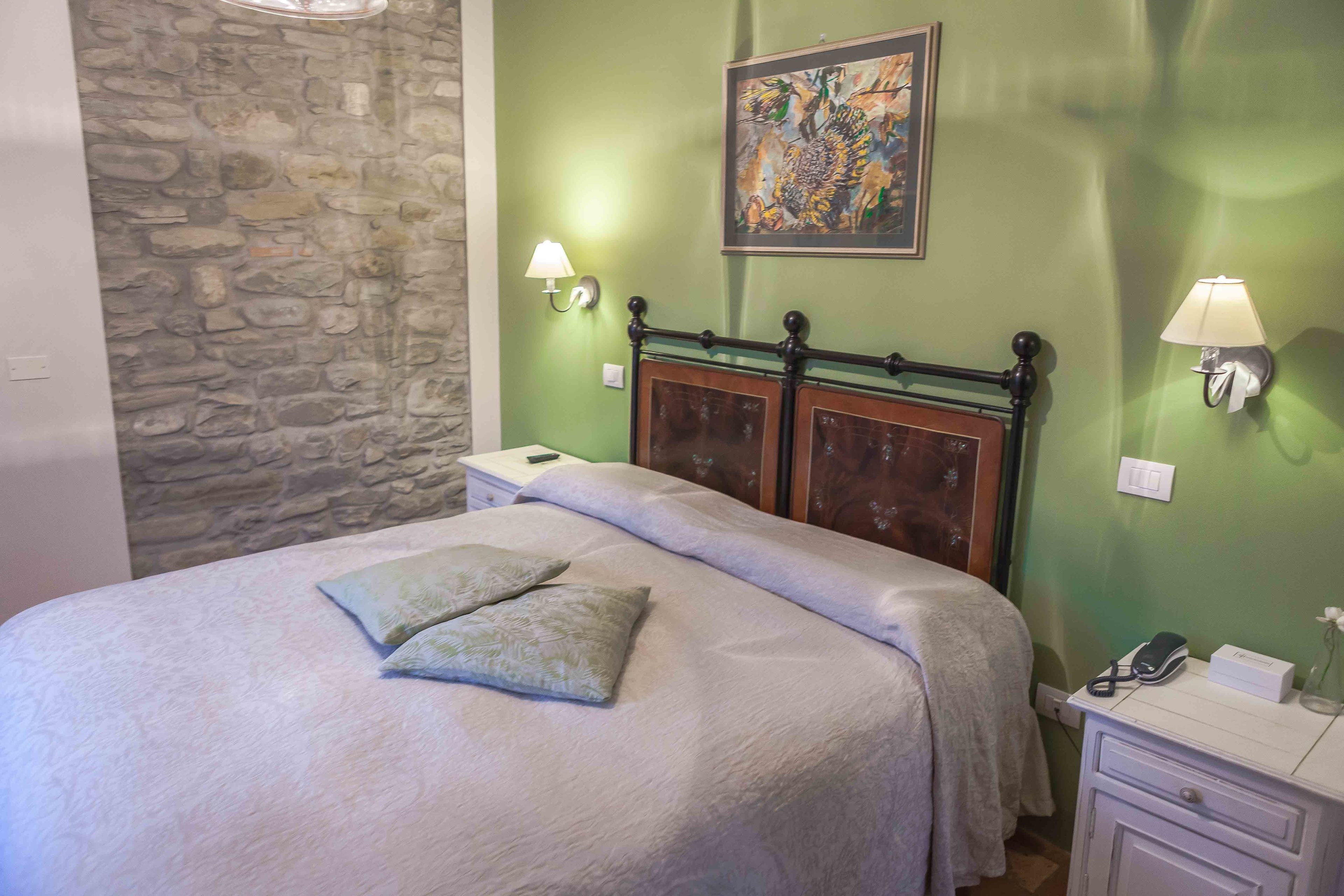 Une chambre avec un mur en pierre, un lit doté d’une tête de lit en bois, deux lampes de chevet et un tableau accroché au mur.