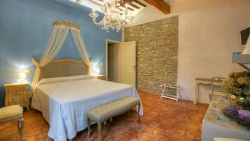 A bedroom with a bed, bench, nightstand, and a stone wall.