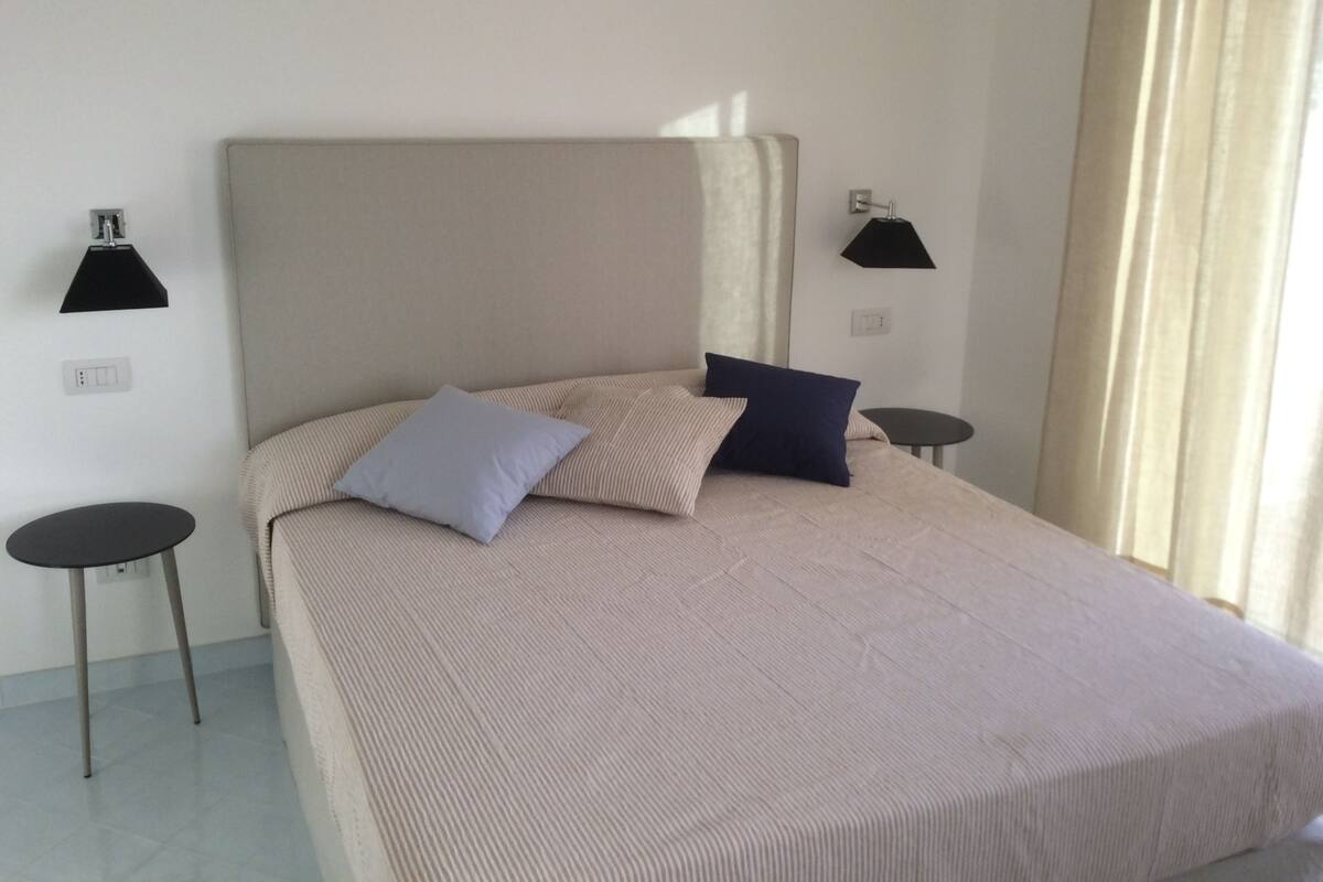 A bedroom with a large bed, two bedside tables, and a window with curtains.
