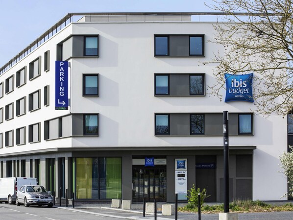 A modern building with a sign for 'ibis budget hotels' and a parking sign indicating a parking area. - ibis budget Saint Quentin en Yvelines Velodrome (Montigny-le-Bretonneux)