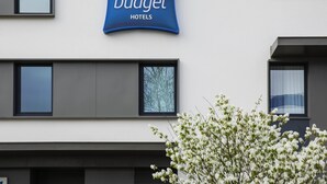 A building with a sign for 'ibis budget hotels' and a tree with white flowers in front. - ibis budget Saint Quentin en Yvelines Velodrome (Montigny-le-Bretonneux)