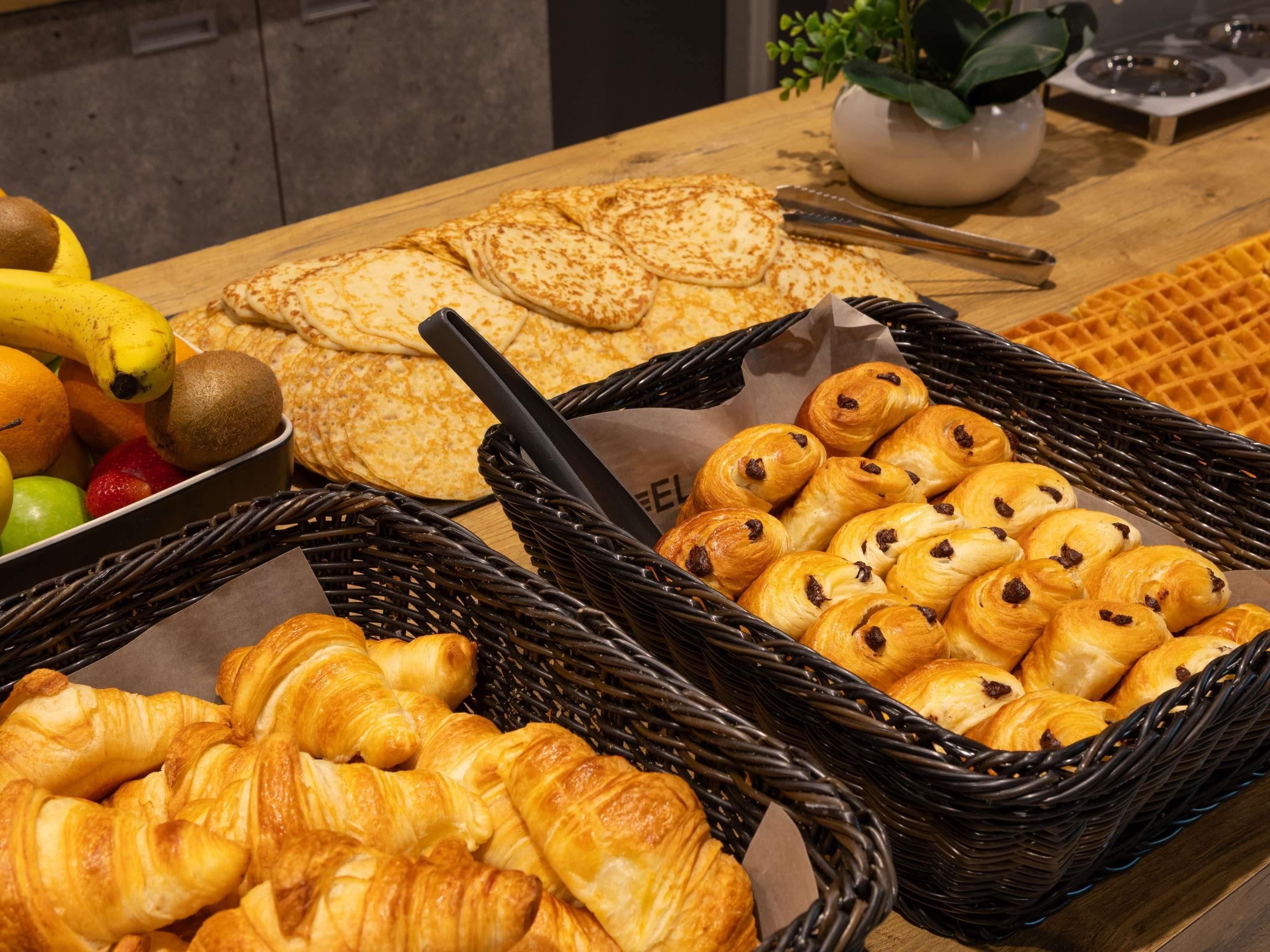 A breakfast buffet with various pastries, fruits, and a waffle.