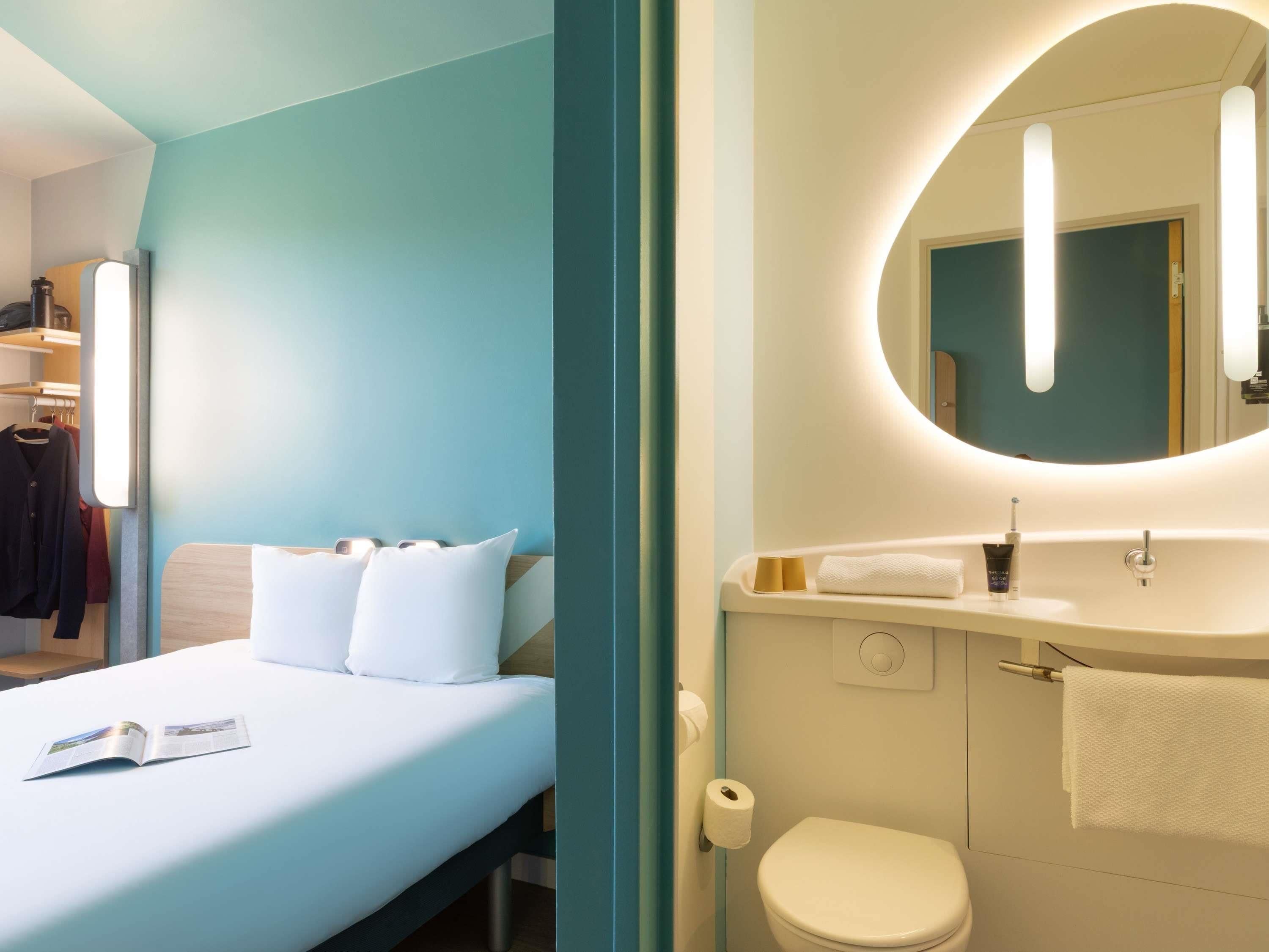 A hotel room with a bed, a bathroom with a toilet, and a mirror.