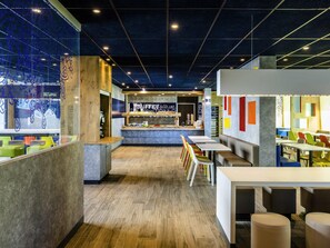 A modern cafe interior with a counter, seating area, and a view through a glass wall. - ibis budget Saint Quentin en Yvelines Velodrome (Montigny-le-Bretonneux)
